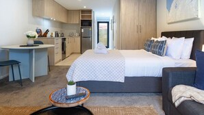A modern hotel room with a bed, a sofa, a small kitchen area, and a dining table. - Modern Studio Near Stadium, Dining & City Fun (Christchurch)