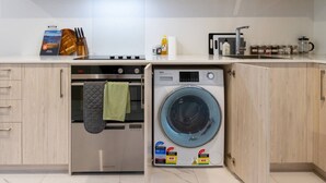 A compact kitchen with a built-in oven, a washing machine, and a coffee maker. - Modern Studio Near Stadium, Dining & City Fun (Christchurch)