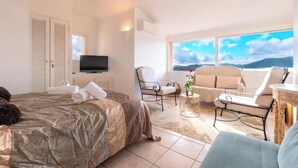 Ein Hotelzimmer mit Bett, Fernseher, Sofa, zwei Stühlen und Blick auf die Berge.
