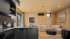 Eine moderne Küche mit integriertem Geschirrspüler, ein Essbereich mit rundem Couchtisch und ein Wohnzimmer mit Sofa und Fernseher.
