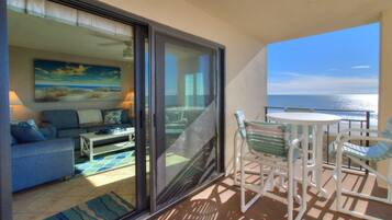 A balcony with a view of the ocean, a seating area with a table and chairs, and a sofa with a painting above it.