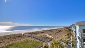 A beachfront hotel with a boardwalk leading to the beach, featuring a view of the ocean and a clear sky.