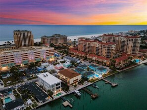 Zona hotelera costera con varios edificios, un puerto deportivo y vista al océano al atardecer.