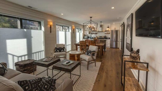A spacious living area with a large window, a dining table, and a kitchen in the background. - Lofts on Main - Ravenel (Highlands)