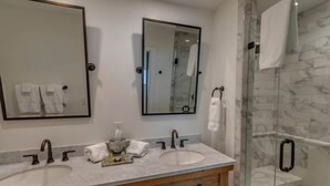 A bathroom with two sinks, a mirror, and a glass shower enclosure. - Lofts on Main - Ravenel (Highlands)