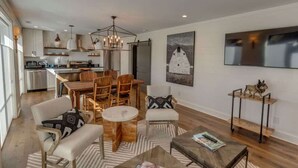 A spacious living area with a dining table, chairs, and a coffee table. There is a kitchen in the background with modern appliances and a chandelier. - Lofts on Main - Ravenel (Highlands)