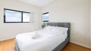Ein modernes Schlafzimmer mit einem großen Bett, einer grauen Kopfteil und zwei Fenstern.