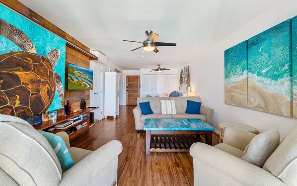 A spacious living area with a wooden floor, a sofa set, and a television mounted on the wall.