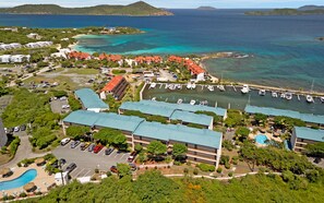 An aerial view of a coastal hotel with multiple buildings, a marina with boats, and a swimming pool.