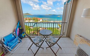 A balcony with a view of the sea and a small island. There is a folding chair and a blue bag on the floor.