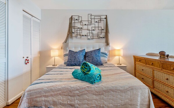 A neatly arranged bedroom with a bed, two bedside lamps, a headboard with a geometric pattern, a wooden dresser, and a wall-mounted decorative piece. - Seconds from Sand & Stunning Sea Views (St Thomas)