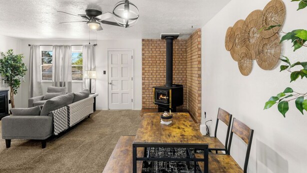 Ein modernes Wohnzimmer mit Kamin, grauem Sofa, Esstisch und Deckenventilator.