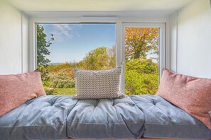 Ein Zimmer mit Blick durch ein Fenster, ein graues Sofa und zwei Kissen.