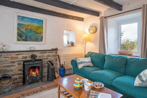 Ein gemütliches Wohnzimmer mit Kamin, einem smaragdgrünen Sofa und einem Tisch mit Tassen und einem Teekessel.