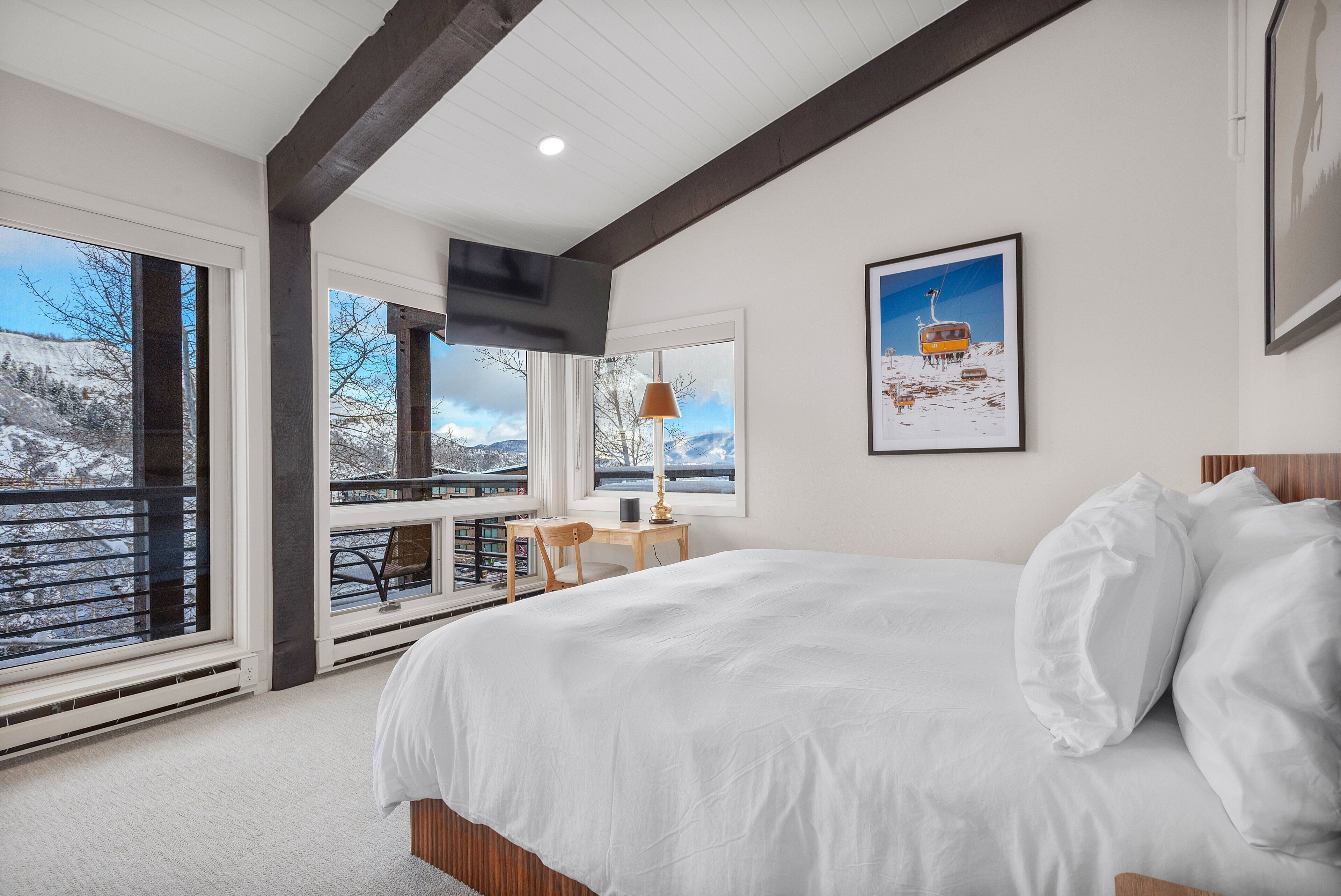 A bedroom with a large bed, a desk, and a window overlooking a snowy landscape.