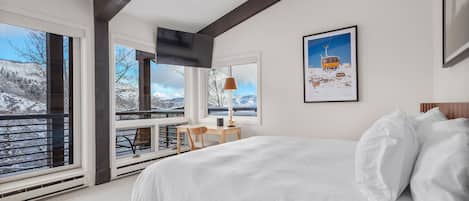 A bedroom with a large bed, a desk, and a window overlooking a snowy landscape.