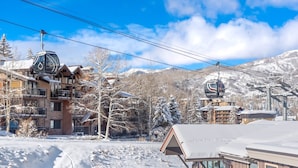 A ski resort with a cable car, snow-covered buildings, and mountains in the background. - Enclave 313 | Ski-In/Ski-Out Condo w/Shared Pool/Hot Tub/Gym/WiFi (Snowmass Village)