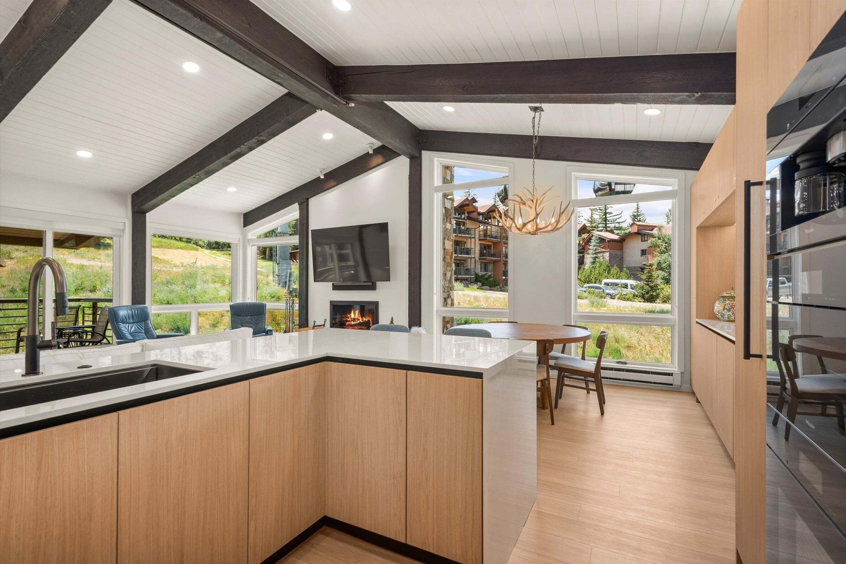 A modern kitchen with a large island, wooden cabinets, and a dining area with a view of the outdoors.