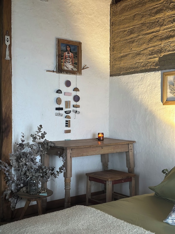 A cozy room with a wooden table, a small stool, a decorative wall hanging, and a framed picture.