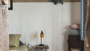 Makuuhuoneessa on sänky, pieni pöytä, jossa on lamppu, seinälle kiinnitetty kasvi ja kehystetty kuva.