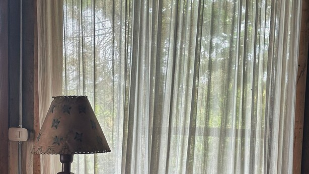 Huoneessa on vanhanaikainen lamppu, pehmusteilla varustettu puinen tuoli ja matkalaukku pöydällä.