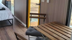 Una habitación moderna con una cama, una mesa de madera con bancos y un ventanal con vistas al exterior.