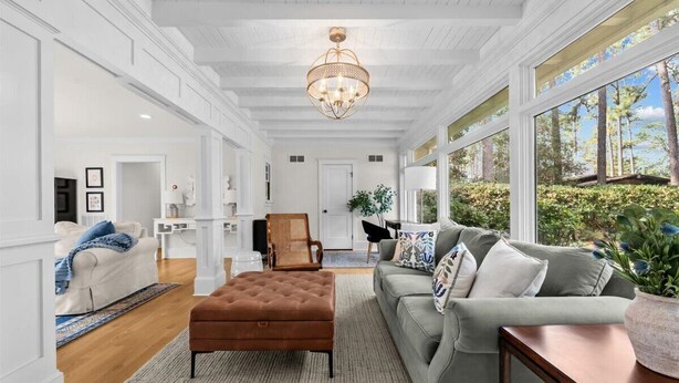 A spacious living room with a large window, a chandelier, and a grey sofa. - Barrett Tee House - Stunning Home in the Village! (Pinehurst)