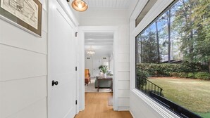 A hallway with white walls, wooden flooring, and a large window overlooking a garden. - Barrett Tee House - Stunning Home in the Village! (Pinehurst)