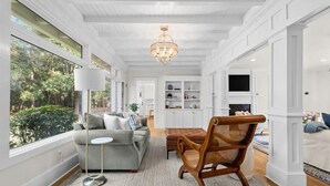 A spacious living room with a grey sofa, a wooden chair, a floor lamp, and a chandelier. - Barrett Tee House - Stunning Home in the Village! (Pinehurst)