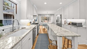 A modern kitchen with white cabinetry, granite countertops, and stainless steel appliances. - Barrett Tee House - Stunning Home in the Village! (Pinehurst)