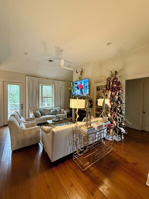 Ein geräumiges Wohnzimmer mit großem Fenster, einem weißen Sofa, einem Couchtisch und einem Weihnachtsbaum.