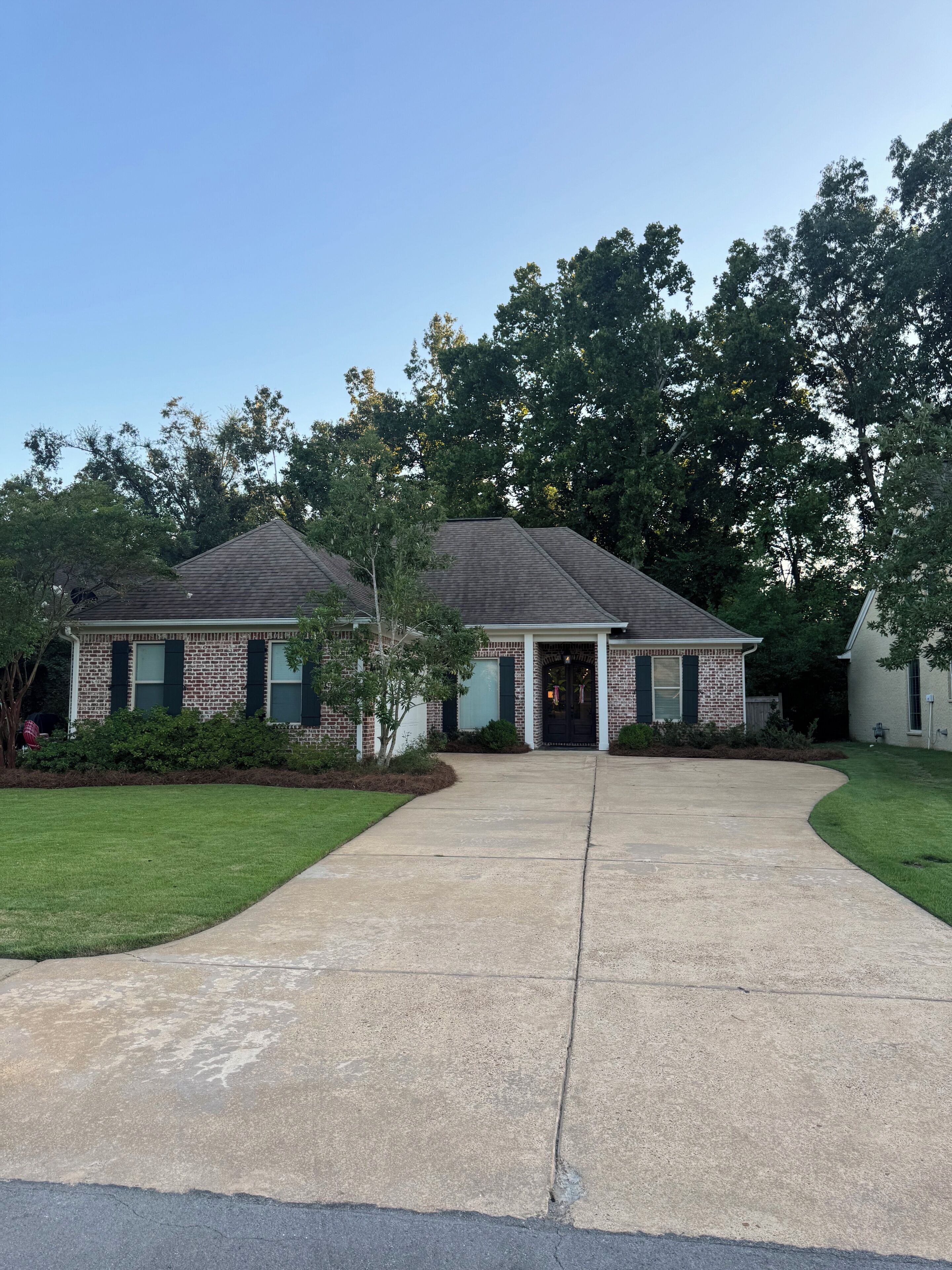 A two-story brick house with a front driveway, a lawn, and trees in the background.