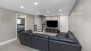 A modern living room with a sectional sofa, a flat-screen TV, and a staircase leading to another room. - Family & Pet Friendly Beach Getaway (Clearwater)