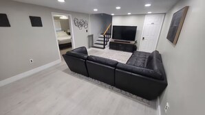 A modern living room with a sectional sofa, a flat-screen TV, and a staircase leading to another room. - Family & Pet Friendly Beach Getaway (Clearwater)