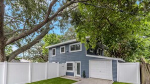 A two-story house with a white garage door, a front yard with a small lawn, and a large tree to the left. - Family & Pet Friendly Beach Getaway (Clearwater)