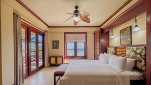 Hotelkamer met een bed, een plafondventilator, een raam met uitzicht op het strand en een deur naar een balkon.