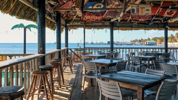 Ein Restaurant im Freien mit Holztischen und -stühlen, einem Reetdach und Blick auf das Meer.