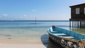 Eine Holzkonstruktion mit einem daran festgebundenen Boot, ein sauberer Strand und ruhiges Meer.