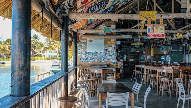 A beachside restaurant with outdoor seating, a thatched roof, and various signs and posters on the walls. - 1BR/1BTH Sea View Suite | Cobia 503 | La Beliza (San Pedro)