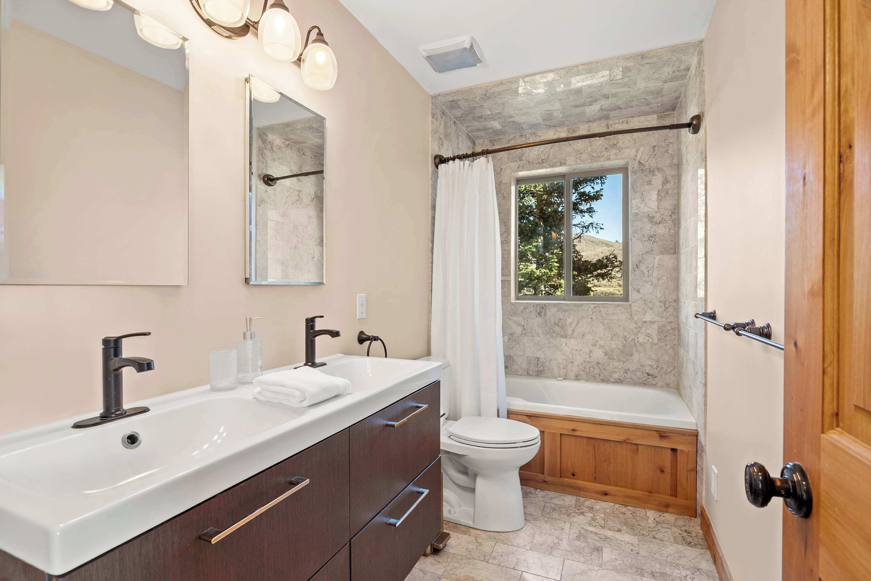 A modern bathroom with a large sink, two faucets, a mirror, a toilet, and a bathtub.