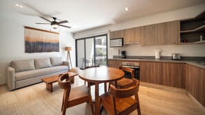A modern kitchen with wooden cabinets, a dining area with a round table and chairs, a sofa, and a ceiling fan. - Depa Moderno con Alberca Tulum 1 Rec (Tulum)