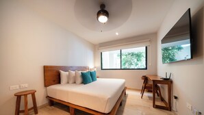 A bedroom with a wooden bed, a small wooden stool, a desk, and a TV mounted on the wall. - Depa Moderno con Alberca Tulum 1 Rec (Tulum)