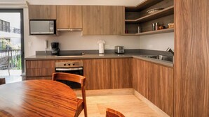A modern kitchen with wooden cabinetry, a built-in microwave, and a dining area with a wooden table and chairs. - Depa Moderno con Alberca Tulum 1 Rec (Tulum)