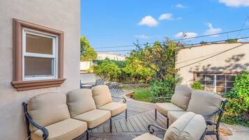 An outdoor patio with a wooden deck, two beige cushioned chairs, and a small table.