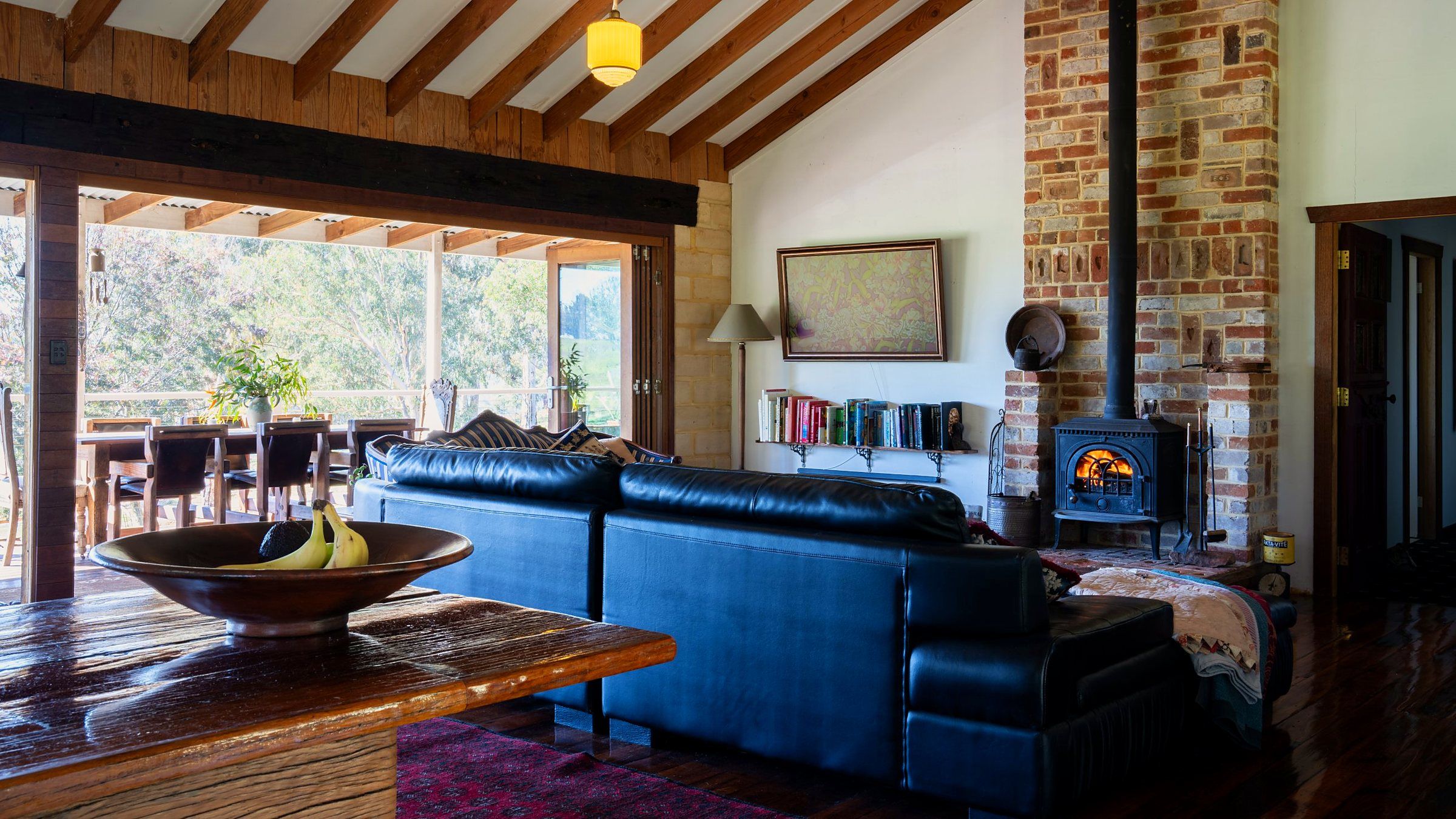 A cozy living room with a leather sofa, a wooden coffee table with a bowl of fruit, a bookshelf, and a brick fireplace.