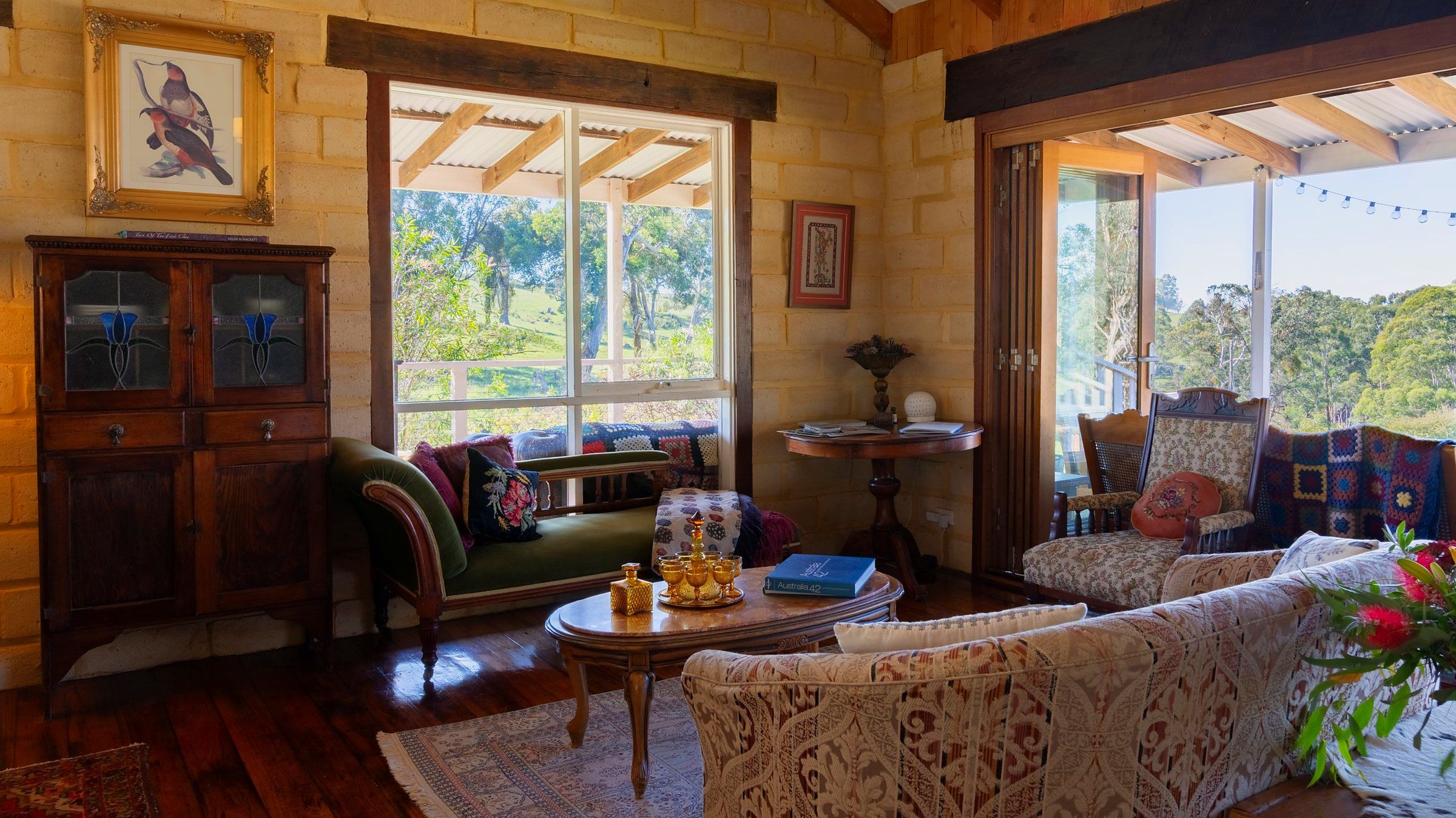 A cozy living room with a large window, a wooden cabinet, a sofa, and a table with decorative items.
