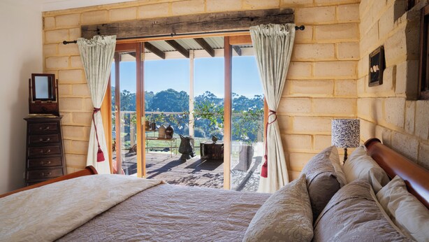 A bedroom with a bed, a dresser, a window with curtains, and a view of greenery.