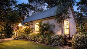 Une maison avec un toit en pente, de grandes fenêtres et un jardin bien entretenu, agrémenté de plantes à fleurs et d’une pelouse.