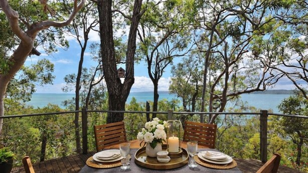Une table en bois, dressée pour le repas, avec vue sur la mer et les arbres.