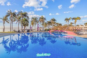 Una piscina con palme, sedie a sdraio, un ponte e un cartello con la scritta 'Beach Please'.